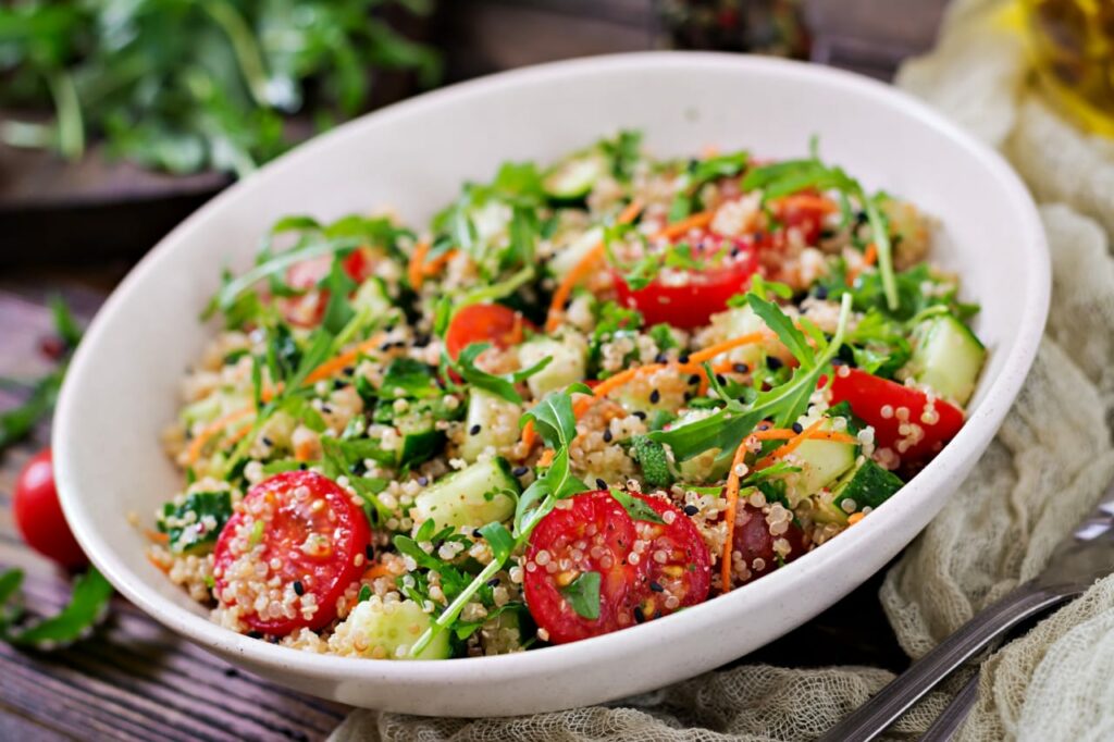 Ancient grains used to make salad, the image shows salad made up of quinoa with vegetables liek tomato, carrots, cucumber etc.